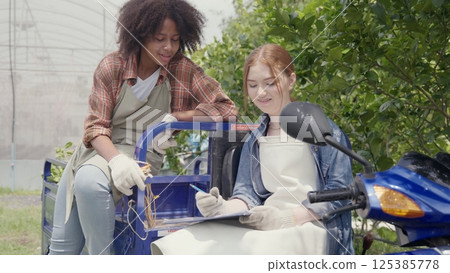 Happy children girl farmer sitting on tricycle in hydroponics farm talking together with worker to take notes on clipboard, Biotechnology kid with Skylab motorcycle transportation at vegetable farm 125385778