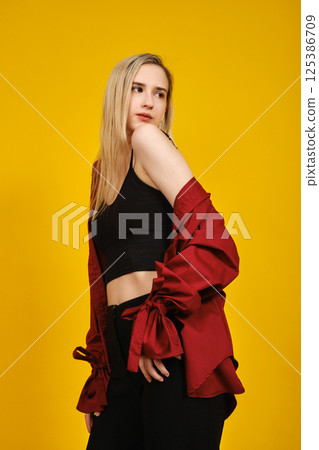 Blonde young woman in a black crop top and a flowing red blouse looks over her shoulder Blonde young woman in a black crop top and a flowing red blouse looks over her shoulder 125386709