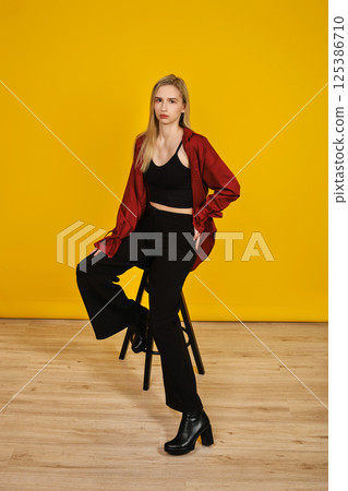 Stylish model poses confidently on a stool against a vibrant yellow backdrop 125386710
