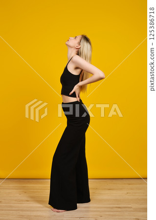 Model posing in black outfit against vibrant yellow background in studio setting 125386718