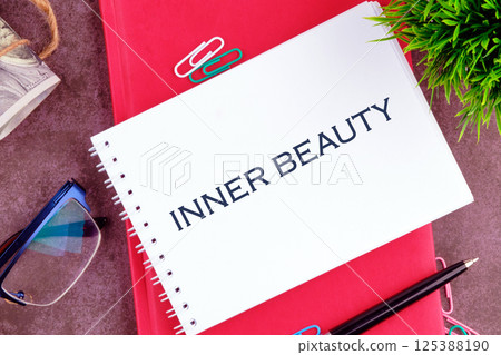 A white notebook reading inner beauty sits on a red background, accented by green paperclips and a small plant, symbolizing mindfulness and personal growth in a calm setting 125388190