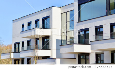 Modern architecture of urban residential apartment buildings on a sunny day. Low-rise apartment buildings with large windows and extensive terraces. White facade of a modern apartment building. 125388347