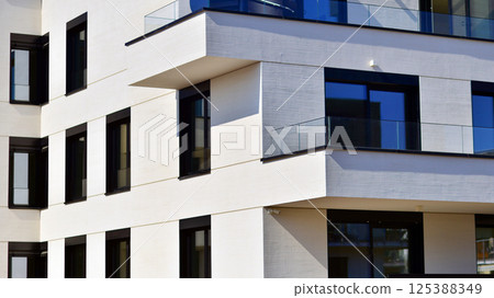Modern architecture of urban residential apartment buildings on a sunny day. Low-rise apartment buildings with large windows and extensive terraces. White facade of a modern apartment building. 125388349