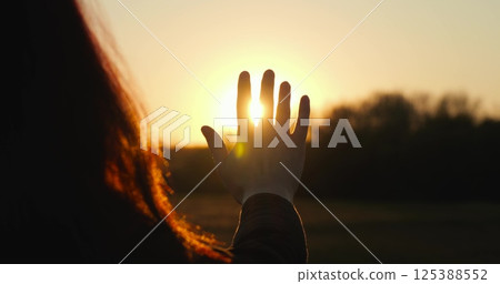 female silhouette sunset stretches out her hand to sun, personifying sustainability and care for nature, ecology and life in harmony with the Earth. palm catches rays sun during sunset close-up. female silhouette sunset stretches out her hand to sun, personifying sustainability and care for nature, ecology and life in harmony with the Earth. palm catches rays sun during sunset close-up. 125388552