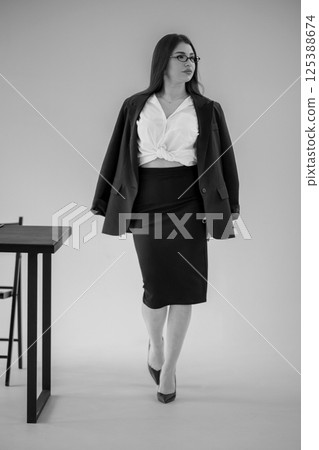 Professional woman walking in modern office space, wearing black suit and white top, serious expression 125388674