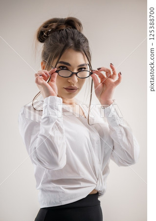 Young woman with glasses adjusting them while looking at camera, professional attire Young woman with glasses adjusting them while looking at camera, professional attire 125388700