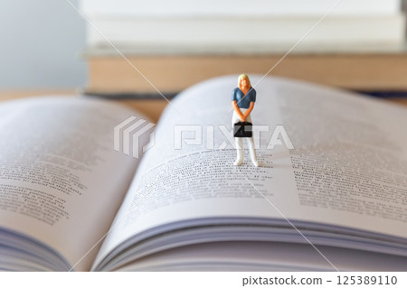 一本打開的英文書和桌上的一個女性身影,學習、學習、再學習的形象 一本打開的英文書和桌上的一個女性身影,學習、學習、再學習的形象 125389110