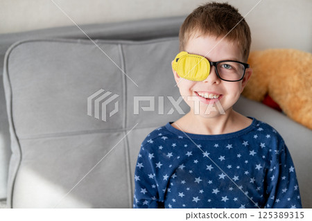 portrait of little boy wearing glasses with occluder to correct vision sitting on sofa at home portrait of little boy wearing glasses with occluder to correct vision sitting on sofa at home 125389315