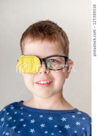portrait of a little boy wearing glasses with an occluder to correct his vision 125389316