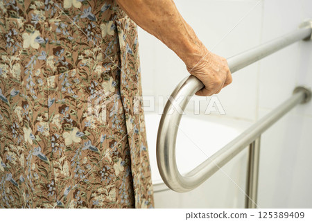 Asian elderly woman patient use toilet support rail in bathroom. 125389409