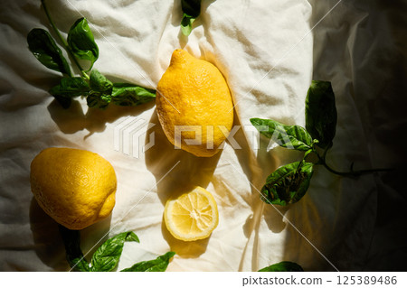 Bright yellow lemons and fresh basil leaves create a vibrant summer arrangement in Italy 125389486