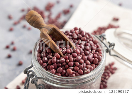Glass jar full of dried azuki beans with a wooden scoop closeup. Vegetarian protein source 125390527