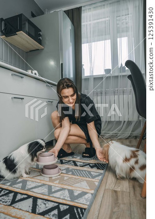 woman caring for japanese chin in modern kitchen, concept of pet care and contemporary lifestyle, vertical 125391430