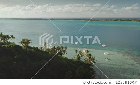 Several boats are sailing on crystal-clear turquoise water near a lush tropical island coastline, creating a picturesque scene of leisure and exploration in a serene paradise 125391507