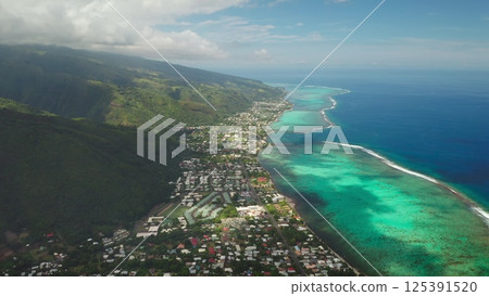 Capturing stunning aerial views of a tropical coastline where lush green mountains meet vibrant turquoise waters, revealing a picturesque town nestled in nature's beauty 125391520