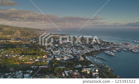 Aerial view of Papeete, the capital city of French Polynesia, showcasing its harbor, cityscape, lush greenery, and the vast pacific ocean during the golden hour 125391522
