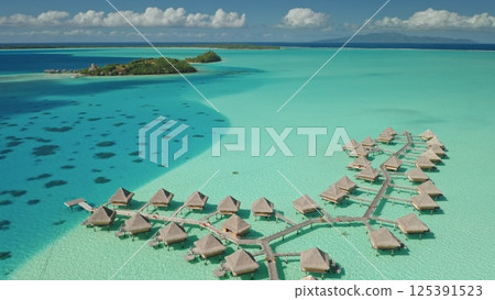 Luxury overwater bungalows resort invite for relaxation and escape. Crystal clear turquoise water, tropical island paradise. Exotic travel vacation getaway, romantic honeymoon. Aerial drone panorama. 125391523