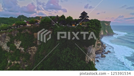 Aerial view capturing Uluwatu Temple perched on a cliff overlooking the ocean at sunset, highlighting its significance as one of Bali's spiritual pillars in Pecatu 125391534