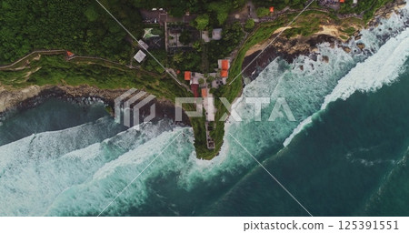Turquoise waves crashing against the cliff where Uluwatu Temple is perched, revealing a breathtaking panorama of Bali's stunning coastline and vibrant natural beauty Turquoise waves crashing against the cliff where Uluwatu Temple is perched, revealing a breathtaking panorama of Bali's stunning coastline and vibrant natural beauty 125391551