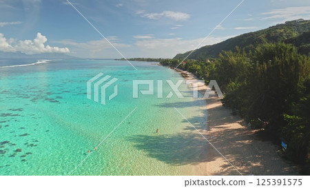 Tourists enjoying crystal clear turquoise water of tropical beach in Tahiti, French Polynesia, lush green vegetation lining the shore, as seen from an aerial drone perspective. Exotic travel vacation Tourists enjoying crystal clear turquoise water of tropical beach in Tahiti, French Polynesia, lush green vegetation lining the shore, as seen from an aerial drone perspective. Exotic travel vacation 125391575