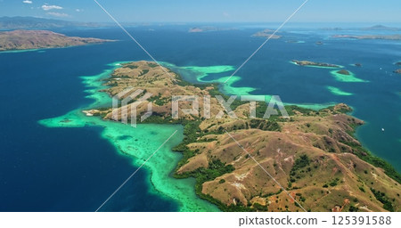 Breathtaking aerial view of Komodo national park in Indonesia, featuring vibrant turquoise waters caressing lush, hilly islands beneath a clear blue sky 125391588