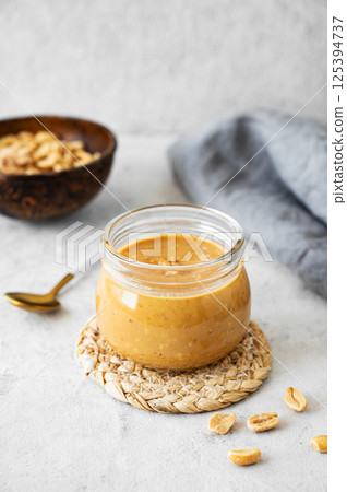 Glass jar  with creamy peanut butter on a wooden board on a grey background 125394737
