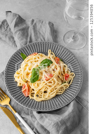 Creamy spaghetti with cherry tomatoes, parmesan cheese and basil on a plate on a light background 125394856