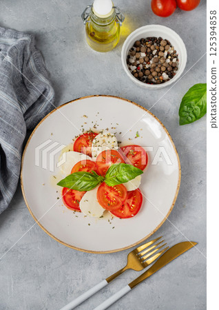Caprese salad with slicedtomatoes, mozzarella and basil on a plate on a light background 125394858
