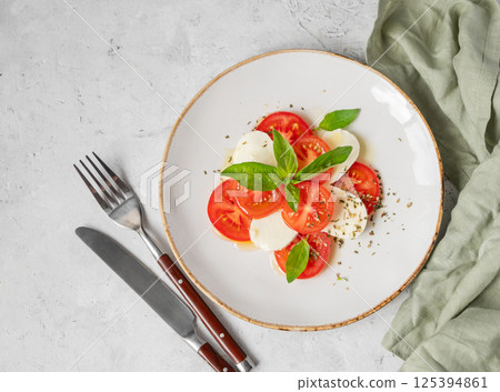 Caprese salad with sliced tomatoes, mozzarella and basil on a plate on a light background 125394861