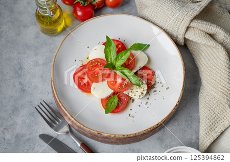 Caprese salad with slice tomatoes, mozzarella and basil on a plate on a light background Caprese salad with slice tomatoes, mozzarella and basil on a plate on a light background 125394862