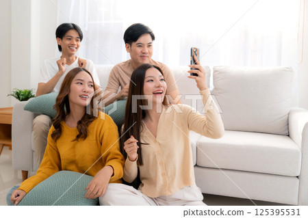 Group young asian friends sitting on sofa taking a selfie or video call using smart phone. 125395531
