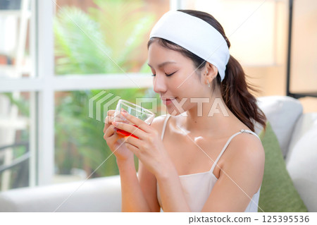 Beautiful young asian woman with headband enjoying tea sitting on sofa with satisfied. Beautiful young asian woman with headband enjoying tea sitting on sofa with satisfied. 125395536