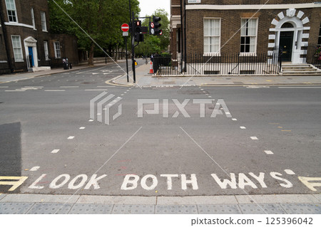 A street in London with the phrase LOOK BOTH WAYS painted on the road, indicating the pedestrian crossing. Traffic lights are visible, showing a red signal, and classic London style buildings A street in London with the phrase LOOK BOTH WAYS painted on the road, indicating the pedestrian crossing. Traffic lights are visible, showing a red signal, and classic London style buildings 125396042