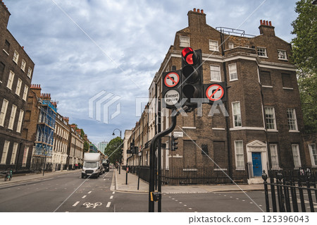 A street in London with a red traffic light and signs indicating no entry except for cycles. The road is lined with classic buildings, and a delivery truck is visible on the street. A street in London with a red traffic light and signs indicating no entry except for cycles. The road is lined with classic buildings, and a delivery truck is visible on the street. 125396043