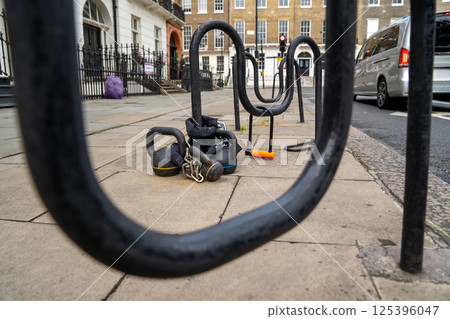A kettlebell is secured to a bike rack on a quiet city sidewalk, drawing attention in the everyday urban scene. A kettlebell is secured to a bike rack on a quiet city sidewalk, drawing attention in the everyday urban scene. 125396047