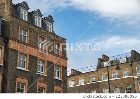 Traditional Terraced Houses Line a Quiet Street with Green Trees and a Red London Bus in View Reflecting the Calm Atmosphere of the Neighborhood. Traditional Terraced Houses Line a Quiet Street with Green Trees and a Red London Bus in View Reflecting the Calm Atmosphere of the Neighborhood. 125396050
