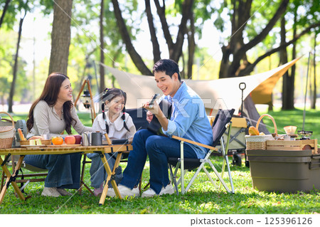 Happy family relaxing and having fun at a wooded campsite Happy family relaxing and having fun at a wooded campsite 125396126