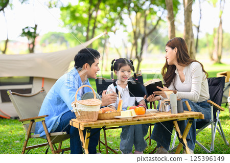 Smiling family reads together during a sunny picnic in the park. Family leisure concept Smiling family reads together during a sunny picnic in the park. Family leisure concept 125396149