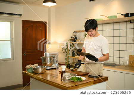 Man using digital tablet by a kitchen island with fresh ingredients, ready to make whipped cream 125396256
