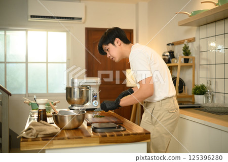 Man wearing black gloves chopping herbs on a wooden cutting board 125396280