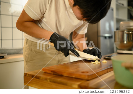 Man wearing black gloves chopping garlic for meal prep in a modern kitchen 125396282