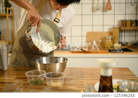 Smiling asian man wearing an apron preparing whipped cream in cozy kitchen 125396288