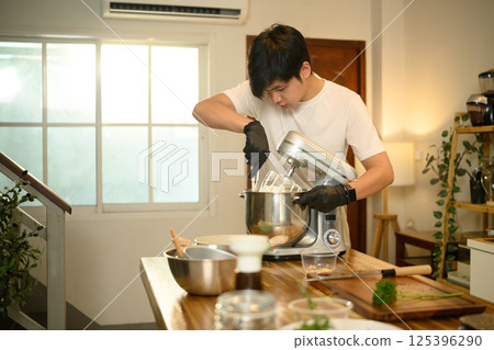 Young asian man in white shirt uses a stand mixer to whip cream in a cozy kitchen 125396290