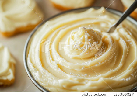 A rich and creamy buttercream frosting swirls high in a wooden bowl. 125396827
