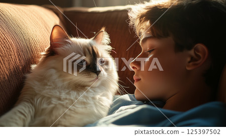 Teenage boy relaxing on couch with his charming ragdoll cat in cozy afternoon setting 125397502
