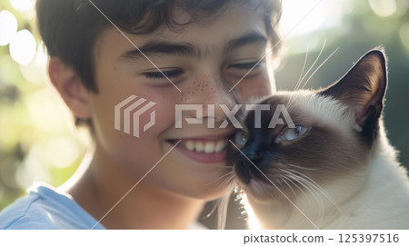 Teenage boy smiles widely while holding a playful cat in a sunlit garden during a cheerful afternoon in early summer 125397516