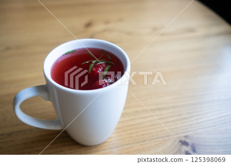 Raspberry tea in a white mug on a wooden table. 125398069