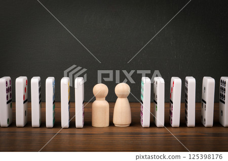 Wooden Figurines Between Falling Dominoes Symbolizing Cause and Effect Wooden Figurines Between Falling Dominoes Symbolizing Cause and Effect 125398176