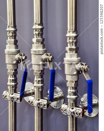 Detailed close-up of industrial piping system with blue handles showcasing valve mechanisms and stainless steel fittings Detailed close-up of industrial piping system with blue handles showcasing valve mechanisms and stainless steel fittings 125398207