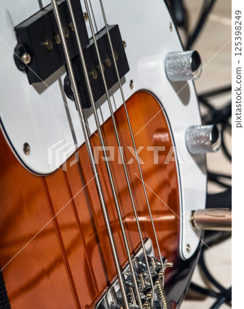 Close-up of electric bass guitar showcasing strings, knobs, and body design in a music studio setting Close-up of electric bass guitar showcasing strings, knobs, and body design in a music studio setting 125398249